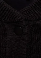 Chaqueta negra de punto con corte bomber, cierre frontal con botones a presión, bolsillos laterales y ribete blanco en cuello, puños, ruedo y hombros.
