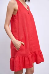 Vestido corto sin mangas, color celeste claro, con escote en V y un pequeño broche decorativo en la abertura frontal. Presenta un corte holgado tipo babydoll con bolsillos laterales y un ruedo con volado.