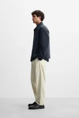 Pantalón chino color beige, corte recto, con bolsillos laterales y traseros. Cierre frontal con cremallera y botón.