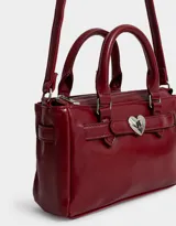 Cartera mini city de cuerina color rojo, con doble asa corta, correa regulable y desmontable, cierre superior y broche metálico de corazón.