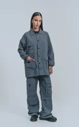 Campera gris con broches en el delantero, forrada con red, múltiples bolsillos con detalles en réflex y puños elásticos en las mangas. Confeccionada en textil liviano 100% poliéster y calce oversize.