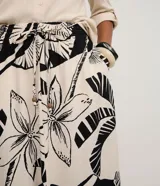 Pollera larga (midi) de corte evasé, con cintura elástica y lazo. Presenta un estampado grande en blanco y negro de motivos tropicales como hojas de palmera y flores.