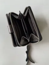 Billetera de cuero color plateado con cierre metálico, cuenta con múltiples compartimentos para tarjetas, billetes y monedas.