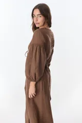 Vestido color beige de lino, con escote en V, mangas largas abullonadas y lazos frontales. Tiene corte a la cintura y falda larga con tajo frontal.