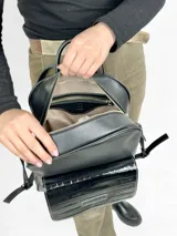Mochila grande de cuero negro con bolsillo frontal de charol y cierre superior.