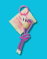 Llavero con aro rosado, etiqueta de tela color crema con texto y logo, cuenta de madera clara y cordón trenzado a rayas turquesa y fucsia.