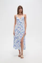 Vestido largo confeccionado en viscosa con estampado floral azul sobre fondo blanco. Posee escote en V, tirantes finos, cintura elástica y una abertura lateral profunda en la falda.