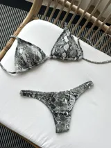 Bikini blanco de lycra texturizada, compuesto por un corpiño de triángulos movibles con tiras finas para atar al cuello y espalda, con almohadillas desmontables, y una bombacha colaless con laterales fijos.