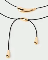 Gargantilla con cordón negro y dije dorado en forma de lágrima.