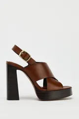 Sandalias de cuero color marrón con plataforma y tacón cuadrado. Tiras cruzadas en la parte delantera y cierre mediante tira trasera con hebilla lateral.