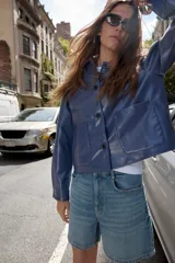 Cazadora azul de cuello solapa y manga larga. Tiene bolsillos de parche en el delantero y cierre frontal con botones.