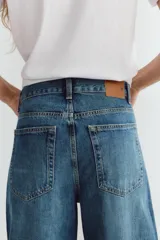 Jeans de tiro medio color azul denim, corte baggy, con trabillas y cinco bolsillos. Cierre frontal asimétrico con cremallera y botones metálicos.