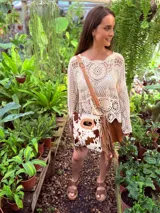 Bandolera de cuero con estampado animal print de vaca en tonos marrón y blanco, con flecos de cuero marrón en los laterales. Tiene correa larga de cuero marrón regulable y asa de mano con forma ovalada.