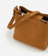 Cartera de gamuza color tostado, de tamaño mediano, con diseño transversal y asa larga ajustable. Cuenta con cierre superior de botón a presión, compartimento interno principal y detalles laterales con ojales metálicos.