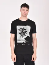 Remera negra de manga corta con estampado rectangular blanco con una palmera, una cabaña y la frase "RELAX TIME / FREE YOUR MIND".