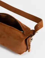 Bandolera color marrón camel de cuerina con textura gamuzada, asa corta de hombro y charm lateral.