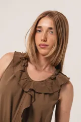 Vestido midi marrón, sin mangas, con volados en el escote y en el ruedo. Presenta un detalle de lazo o tiras de tela que caen desde el cuello.