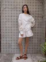 Buzo de algodón color blanco roto, de corte holgado, con puños y tajos laterales. Presenta un bordado artesanal en relieve de líneas orgánicas en color marrón caramelo sobre las mangas.