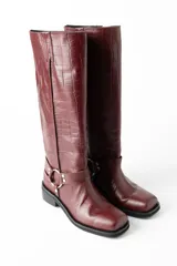 Botas de cuero color bordó con textura croco, caña alta con correa decorativa con argolla metálica y taco bajo.