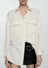 Camisa color crema de lino y lyocell, de corte oversize, manga larga con puños abotonados, cuello camisero, cierre frontal con botones ocultos y dos bolsillos de parche en la parte delantera.