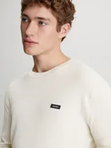 Sweater de punto color crema, de corte recto, con cuello redondo y logo de Calvin Klein en el pecho.