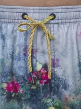 Short de baño verde con estampado de margaritas blancas y cordón ajustable naranja.