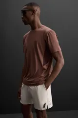 Camiseta deportiva marrón de corte relaxed fit, cuello redondo y manga corta. Presenta paneles laterales de malla negra y logo estampado en la espalda.
