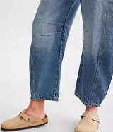 Jean de denim azul claro con lavado desgastado, tiro medio y pierna ancha. Presenta roturas y paneles con costuras visibles en la parte delantera de las piernas.