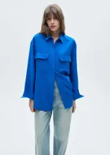 Camisa azul eléctrico de tejido fluido con mezcla de lino y lyocell, cierre frontal oculto, manga larga con puños abotonados, diseño recto, cuello camisero, diseño largo y dos bolsillos de solapa en la parte delantera.