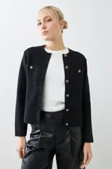 Chaqueta tejida negra con cuello redondo, cierre frontal con botones dorados, bolsillos delanteros y corte clásico.
