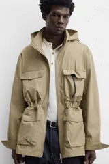 Parka color beige de tejido técnico ligero, corte relaxed fit, cuello alto con capucha plegable, manga larga con puños ajustables con botón a presión, cierre frontal con cremallera, cintura ajustable con elástico interno y múltiples bolsillos frontales de parche con solapa.