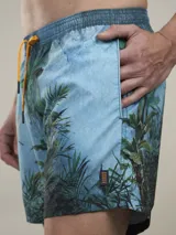 Short de baño verde con estampado de margaritas blancas y cordón ajustable naranja.