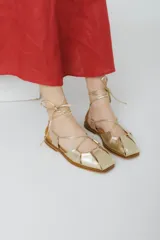 Sandalias bajas de cuero color marrón con tiras finas que se atan al tobillo.