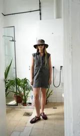 Vestido corto de jean gris con botones frontales, sin mangas, con cuello camisero y bolsillos en el pecho.