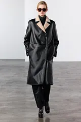 Abrigo largo de Zara Woman Collection, confeccionado en tejido efecto piel color negro. Tiene cuello solapa, manga larga, bolsillos laterales ocultos y forro interior de borreguillo color beige. El cierre es cruzado con botones.