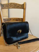 Cartera con estampado animal print de vaca en blanco y negro, con cierre metálico dorado y correa de cadena metálica.