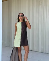 Minivestido sin mangas con escote recto y corte evasé. Presenta un diseño bicolor con una mitad en verde claro y la otra en marrón oscuro. Tiene bolsillos laterales ocultos y cierre en la espalda.