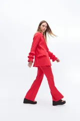 Conjunto de blazer y pantalón acampanado color rojo. El blazer es de corte clásico con solapas y un botón, y tiene volados en las mangas. El pantalón es de tiro alto y pierna acampanada.