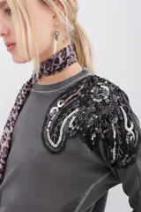 Buzo gris de algodón rústico con mangas dolman y cuello redondo. Apliques bordados con mostacillas y lentejuelas en los hombros.