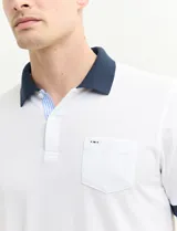 Remera polo blanca de piqué con cuello y puños en azul marino. Tiene tapeta de dos botones y bolsillo de parche en el pecho.