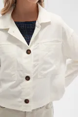Chaqueta color blanco hueso de lino con cuello camisero, cierre frontal con botones marrones, bolsillos de parche en el pecho y corte holgado.