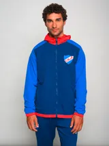 Campera deportiva con capucha, azul con mangas celestes y detalles en rojo. Escudo del Club Nacional de Football bordado en el pecho.