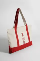 Bolso tipo totebag de lona color crudo con base y asas en color rojo. Estampado frontal con el texto "The Beach Club" en rojo.