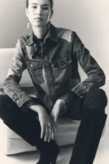 Campera recta de denim rígido con combinación de recortes en distintos tonos de azul, cuello clásico, cierre frontal con botones metálicos, bolsillos con solapa y botones metálicos en el pecho, y mangas largas con puños abotonados.