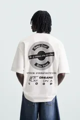 Camiseta blanca de corte holgado, cuello redondo y manga corta. Estampado frontal y trasero con gráficos y textos combinados en color negro.