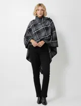 Capa corta de tejido grueso, color verde esmeralda con diseño de cuadros escoceses en azul marino y líneas finas en beige. Posee cuello alto que se cruza al frente y se cierra con un broche oscuro.