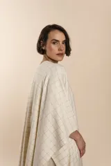 Ruana marrón con diseño a cuadros blancos, terminación envivada y flecos cortos.