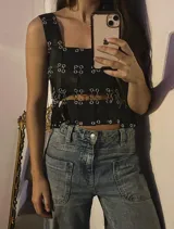 Top negro de cuero genuino de ovino, estilo crop top con tirantes anchos y múltiples aros metálicos plateados que conectan secciones de la prenda, creando aberturas en el torso y abdomen.