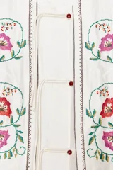 Top blanco de cuello mao y sin mangas, con bordados florales en el frente y cierre con botones.