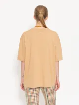 Remera color beige con estampado de figura humana con flores y objetos decorativos.